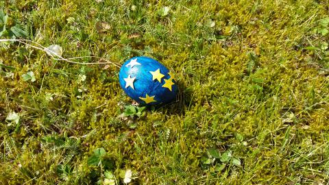 Ein Osterei in den Farben der EU liegt im grünen Gras
